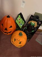 Photo showing two plastic light-up pumpkins, a boxed Wiggling Witch, and a felt Halloween wall hanging with Frankenstein face