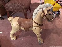 Image of beige plastic Marx Marvel the Mustang vintage riding toy horse with brown saddle and white mane and tail on carpet.
