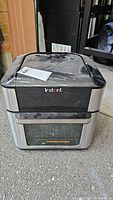 Front view of Instant Pot Vortex 10 Plus air fryer oven showing black and stainless steel exterior with front glass door and logo on the top.