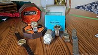 Lot of six men's watches including Bulova Set-o-Matic in original case, two N brand stainless steel watches (one with cracked face), Timex with leather strap, Ottimo and BT watches with stainless steel bands, all on a table.