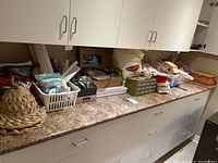 Kitchen countertop with many craft and sewing supplies including baskets, ribbons, batting, and notions