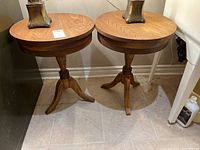 Photo showing both wooden pedestal side tables side by side, highlighting shape and finish.