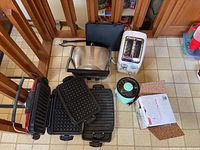 Full view of all items including George Foreman grill, Cuisinart Griddler with waffle and flat grill plates, T-Fal toaster, and Dash mini rice cooker on kitchen floor.