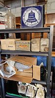 Metal Bell Telephone Company of Canada sign on upper shelf with rotary phones, solvent cans and biscuit tin below
