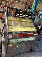 Front right three-quarter view showing wood veneer side panel, illuminated Wurlitzer logo, song selection panel and push buttons