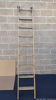 Full view of tall wooden library ladder showing all rungs, leaning against a textured brick wall.
