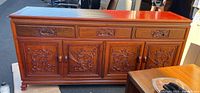 Front view of solid cherry wood credenza with three drawers and four cabinet doors carved with dragon designs, standing outdoors.