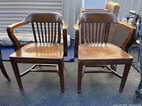 Front view of two solid wood office chairs showing curved arms, slatted backs, and contoured seats with wear.