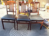 View of 4 folding wood dining chairs with black leather seats showing front and backs.