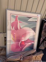 Framed art print showing a large pink lily flower in stylized form with pink, white, gray and teal colors, framed with a white frame and mat with pink border.