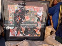 Full view of the framed art showing colorful abstract figures and swirls in a black ridged frame.