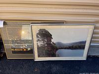 Two framed photos leaning against a wall, showing a lake scene and night cityscape.