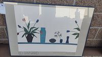 Wide photo showing the full framed poster with modern minimalist style art showing vases and plants, with shadow and reflection visible on the glass.