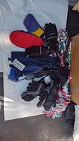 Lot contents showing four pairs of ski gloves, gaiters, and small crocheted afghan alongside ski accessories scattered on white paper.