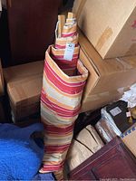 Striped fabric hammock rolled or folded, showing the brightly colored horizontal stripes and wooden bar inside the fabric roll.