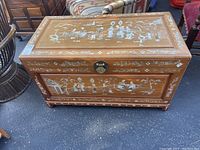 Full frontal view of wooden chest with detailed mother of pearl inlay artwork on top and front panels, showing decorative Asian themed scenes.