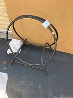 Side angle of black metal fireplace log holder showing round frame and stand with some scratches.