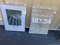 Two metal picture frames 18x24 inches wrapped in plastic and leaning against a wall