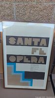 Full view of framed Santa Fe Opera poster with abstract geometric design and text.