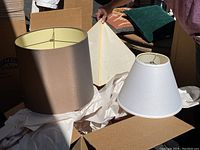 Three lamp shades on display including a dark round silk shade, white conical shade, and beige drum shade.