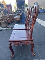 Side view of two of the carved solid cherry wood dining chairs showing cabriole legs and claw feet with floral carvings on seat apron and backrest.