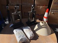 Two metal table lamps with an open rectangular frame design, one beige fabric lampshade, and two wrapped packages containing lamp harps and bulbs.