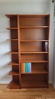 Front view of the two wooden shelves placed side by side against a wall, showing the large shelving unit with books and the narrow shelving unit with open sides.