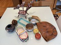 Lot items arranged on white tabletop showing handmade wooden birds, pottery pieces, wooden apples, small sculpture, leaf tray, and artwork.