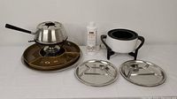 Photo showing complete fondue lot including 'Spring' fondue pot with burner, electric fondue pot with stand, bottle of fondue fuel, and six segmented metal plates