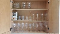 Closely spaced glass shelves in a cabinet displaying all included items in lot, including stemware glasses, side plates, and sorbet bowls.