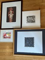 Four framed artworks laid on hardwood floor showing grouping of prints and pastel.