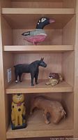 Five hand carved wooden animal sculptures on wooden shelving: duck top, horse and lion middle, cat and buffalo bottom.