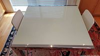 Overhead view of glass top kitchen table showing smooth glass surface and metal frame with part of chairs visible