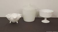 Overall view of three milk glass pieces: candy dish, lidded cookie jar/ice bucket, and fruit bowl.