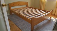 Full view of pine double bed frame showing headboard, footboard and slatted base on carpeted floor.