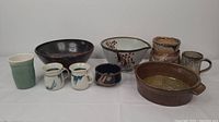 Full view of all 10 pottery pieces including vases, bowls, and mugs on white surface