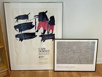 Two framed prints leaning against the wall: larger Cape Dorset art with abstract animal shapes and smaller Oakville Galleries print with intricate line details.