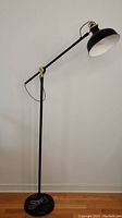 Full view of the Ikea reading floor lamp showing its height, base, adjustable arm and black finish with gold hardware accents.