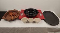 Full view of serving items including red ceramic tray, black ceramic platter, wooden plate, three small bowls and wooden spoons arranged on white cloth for size reference.