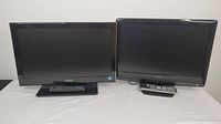Two Toshiba televisions side by side on a flat surface, each with its remote placed in front of or beside them.