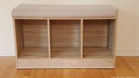 Frontal view of the wooden storage bench showing three cubby compartments and beige cushion seated on top.