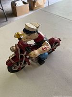 Photo showing the assembled Popeye riding the red patrol motorcycle with clear view of Popeye's sailor hat and arm tattoo
