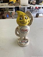 Front view of Mr. Drip cast iron bank figure showing yellow droplet-shaped head, Esso logo on torso and base, smiling facial expression.