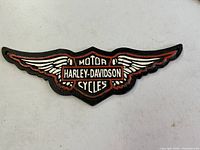 Front view of wing-shaped cast iron sign showing Harley-Davidson Motor Cycles logo in black, red and white