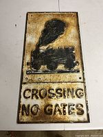 Front view showing entire two-piece cast iron railroad crossing sign with embossed black steam train and 'CROSSING NO GATES' text, surface rust and paint wear visible