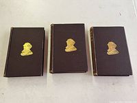 Three volume set of Charles Dickens books laid out showing brown covers with gold embossed silhouette on front