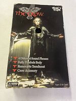 Front view of unopened original box showing The Crow doll packaging with features listed: 4 sound phrases, fully poseable, removable trenchcoat, crow accessory.