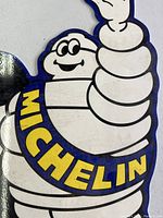 Close-up image of the Michelin Man character and the word 'MICHELIN' on the porcelain sign, showing glossy surface and detailed outlines.