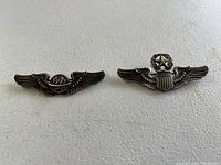 Two WWII sterling silver Air Corps gunner wing medals side by side on a white background with clear detail of design and patina.