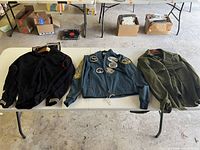 Lot of three military wool clothing items on white table: US Navy shirt, pilot jacket with patches, and green army shirt.